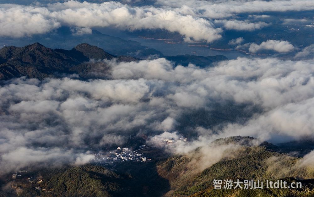 高山之巅俯瞰，云雾如海浪般在层峦间翻涌，山谷里的村庄在云隙间若隐若现，远处湖面泛着微光